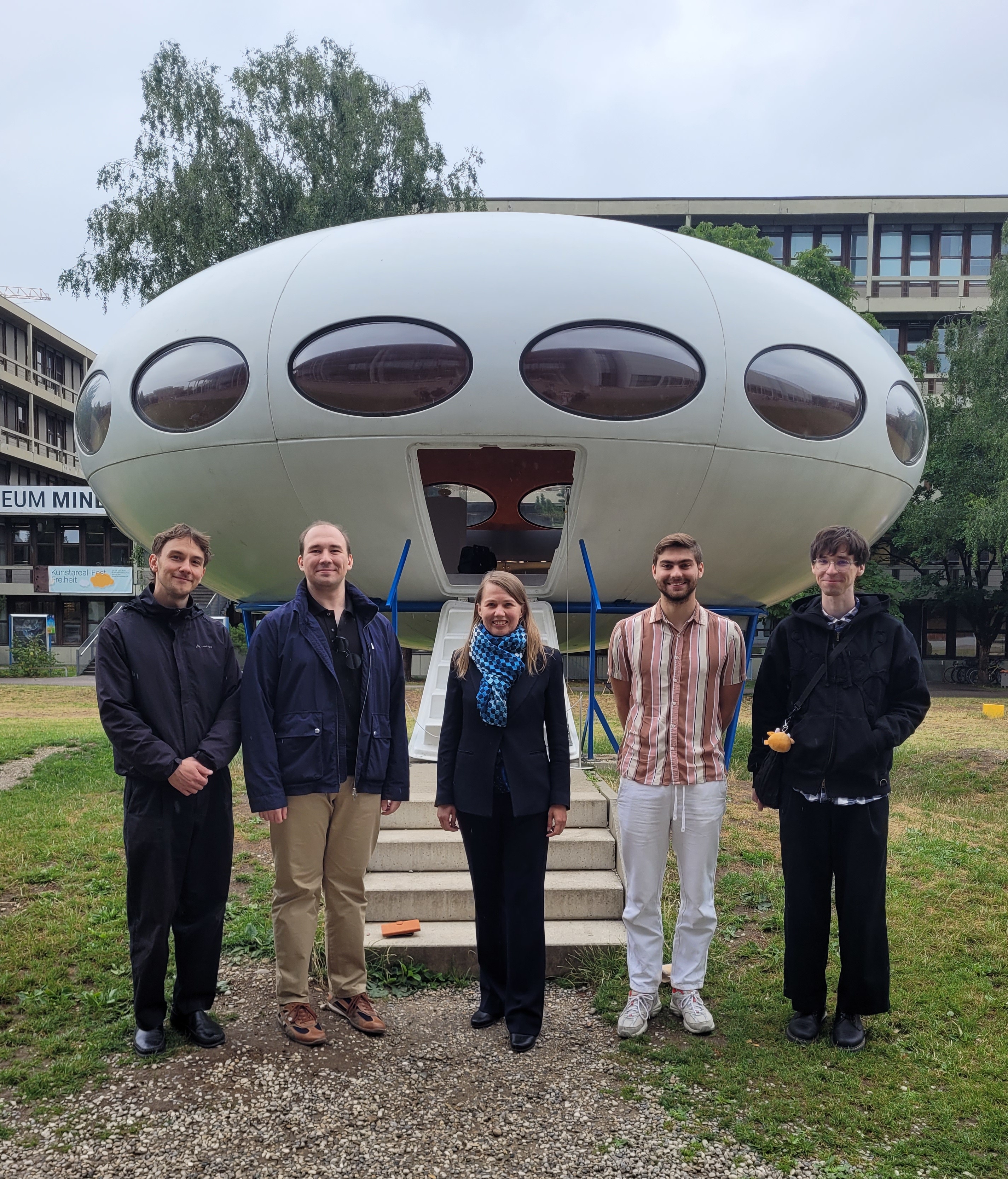 Research group standing in front of a retro-style space capsule